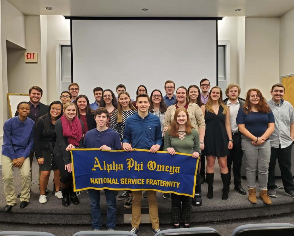 Zeta Alpha chapter of Alpha Phi Omega at Bradley Unversity poses as a group after their Spring 2020 ceremony. Three members in the front row hold a blue banner with gold border and lettering that reads "Alpha Phi Omega National Service Fraternity"